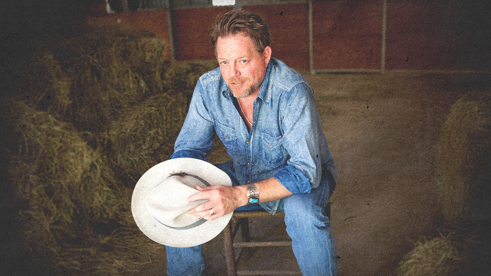 Pat Green sitting on a stool holding a cowboy hat in his hands